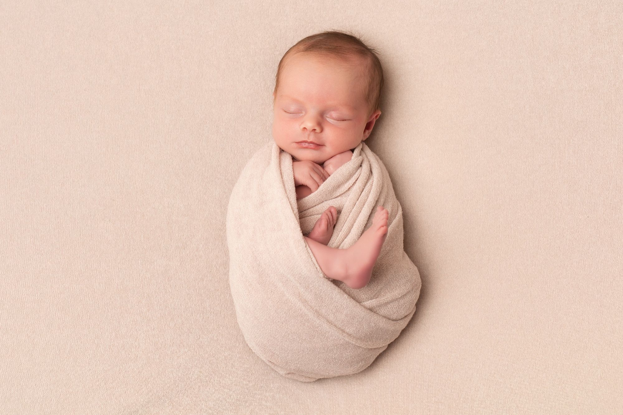 Sleeping newborn swaddled in a beige wrap, newborn photo session at the studio
