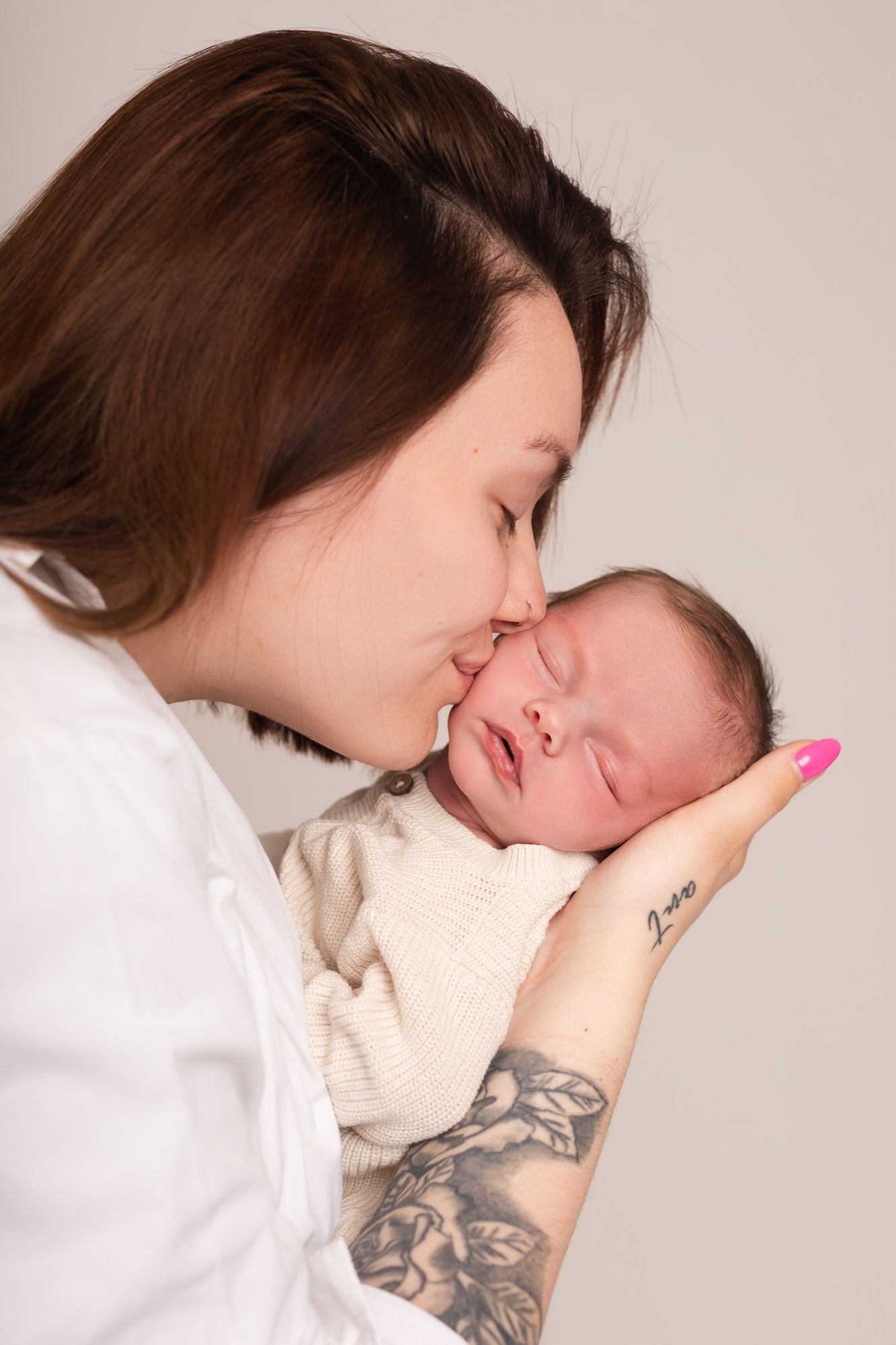 Mother tenderly kissing her sleeping newborn's cheek, newborn photo session at the studio