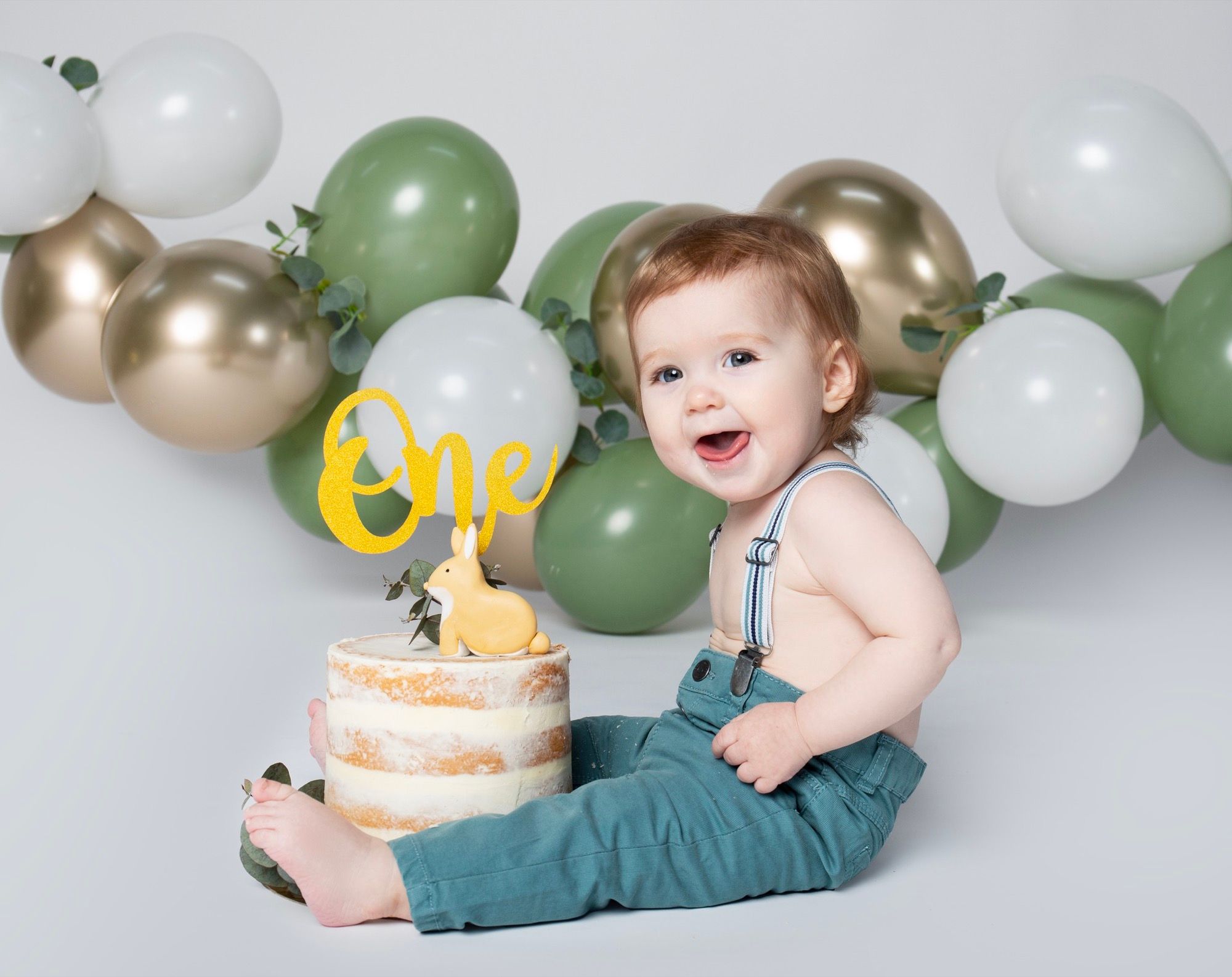 Petit garçon debout parmi des ballons verts et blancs pour son premier anniversaire (1)