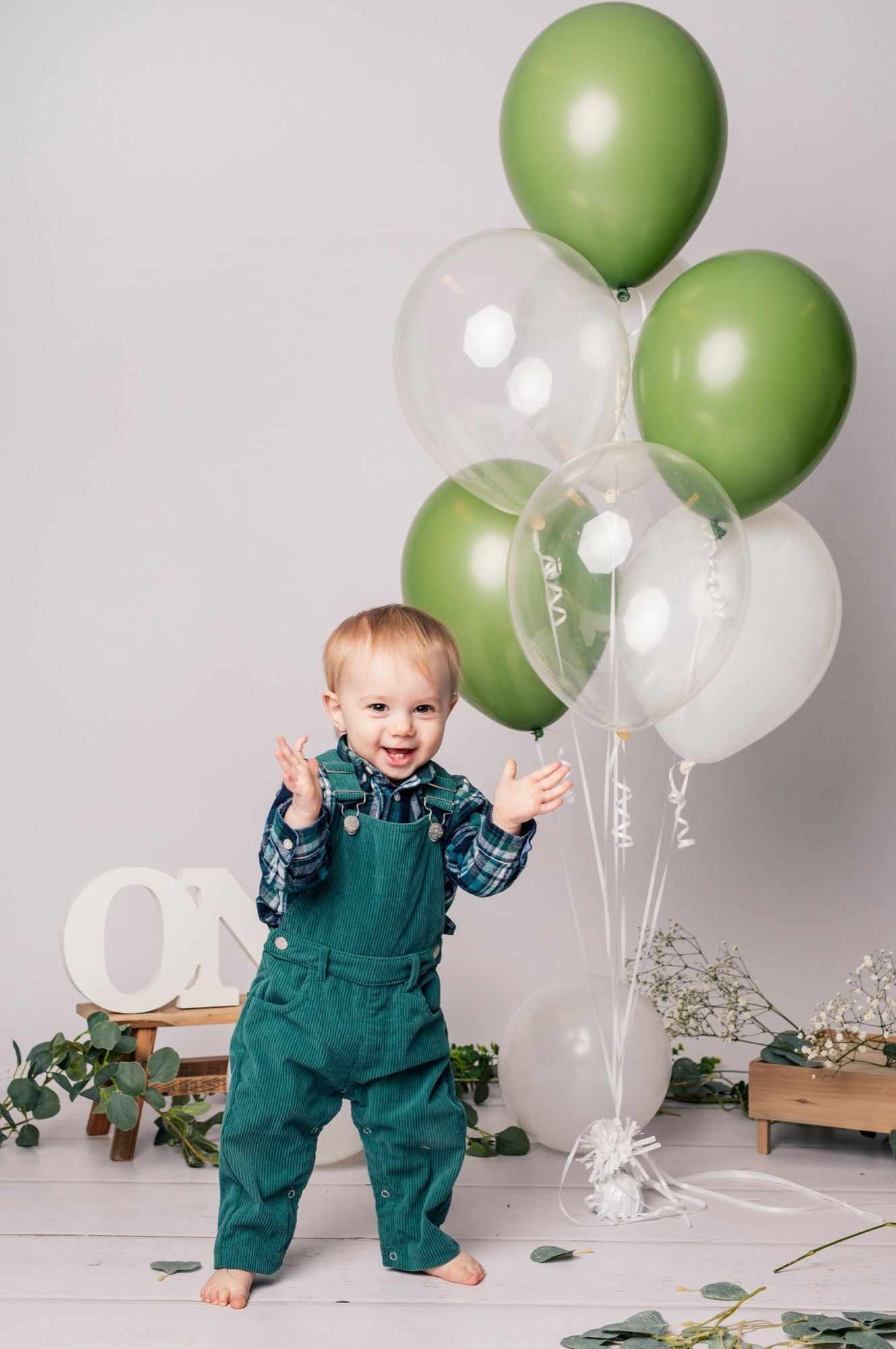 Petit garçon debout parmi des ballons verts et blancs pour son premier anniversaire (5)