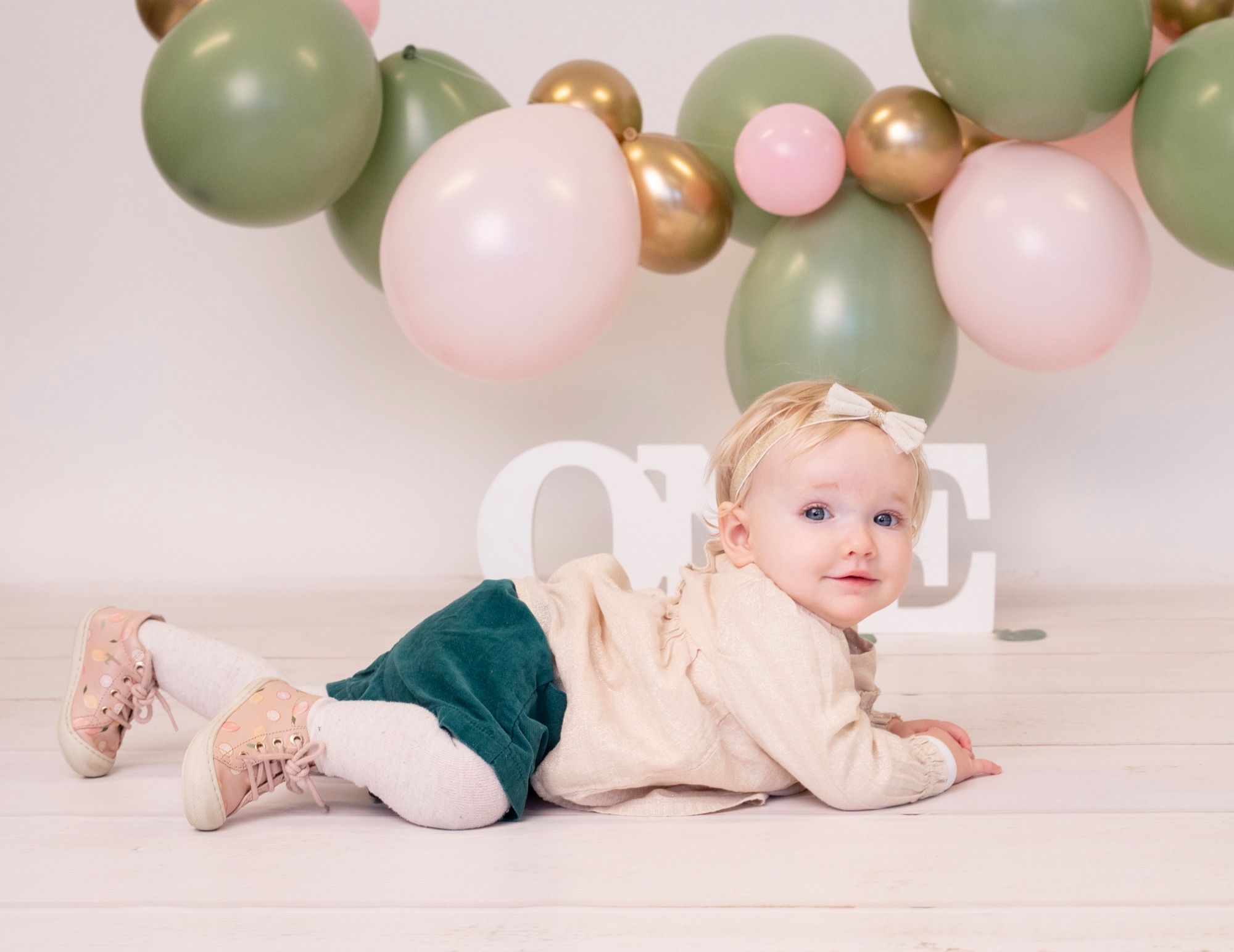 Petit garçon debout parmi des ballons verts et blancs pour son premier anniversaire (8)