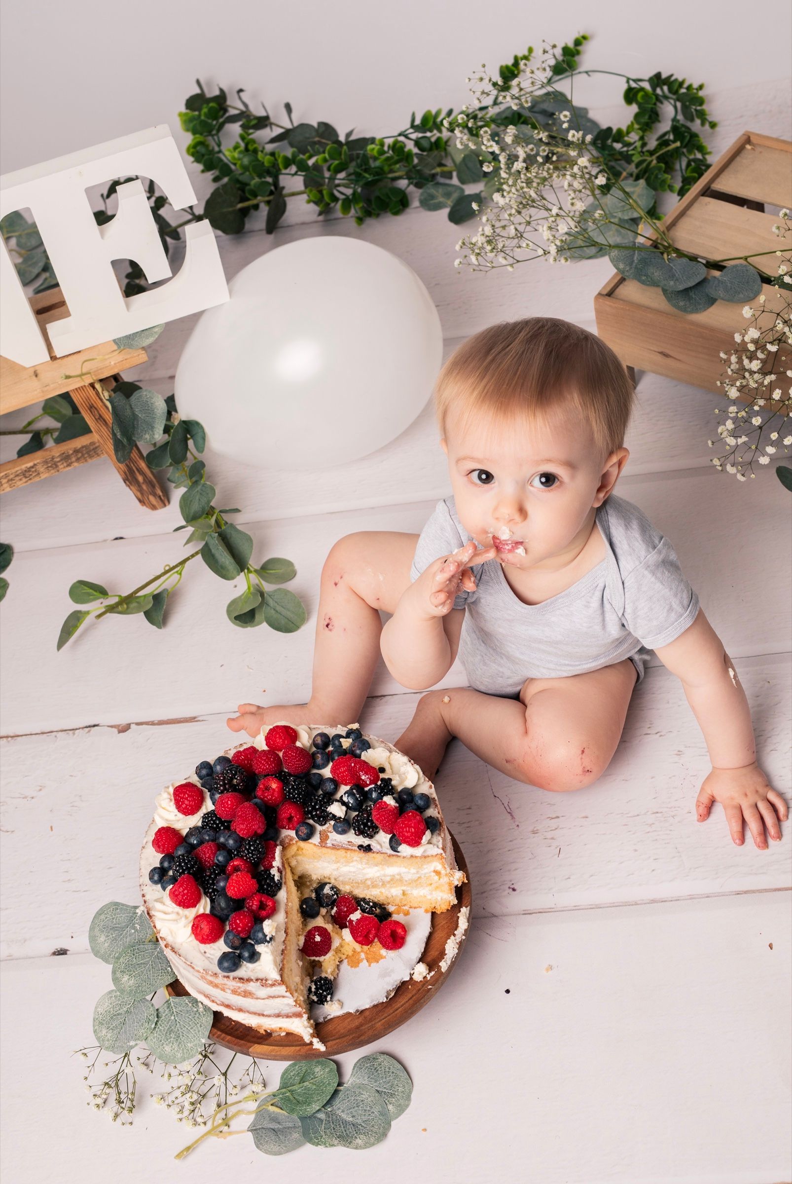 Bébé assis près de son gâteau d'anniversaire aux fruits rouges, décor végétal naturel, premier anniversaire en studio
