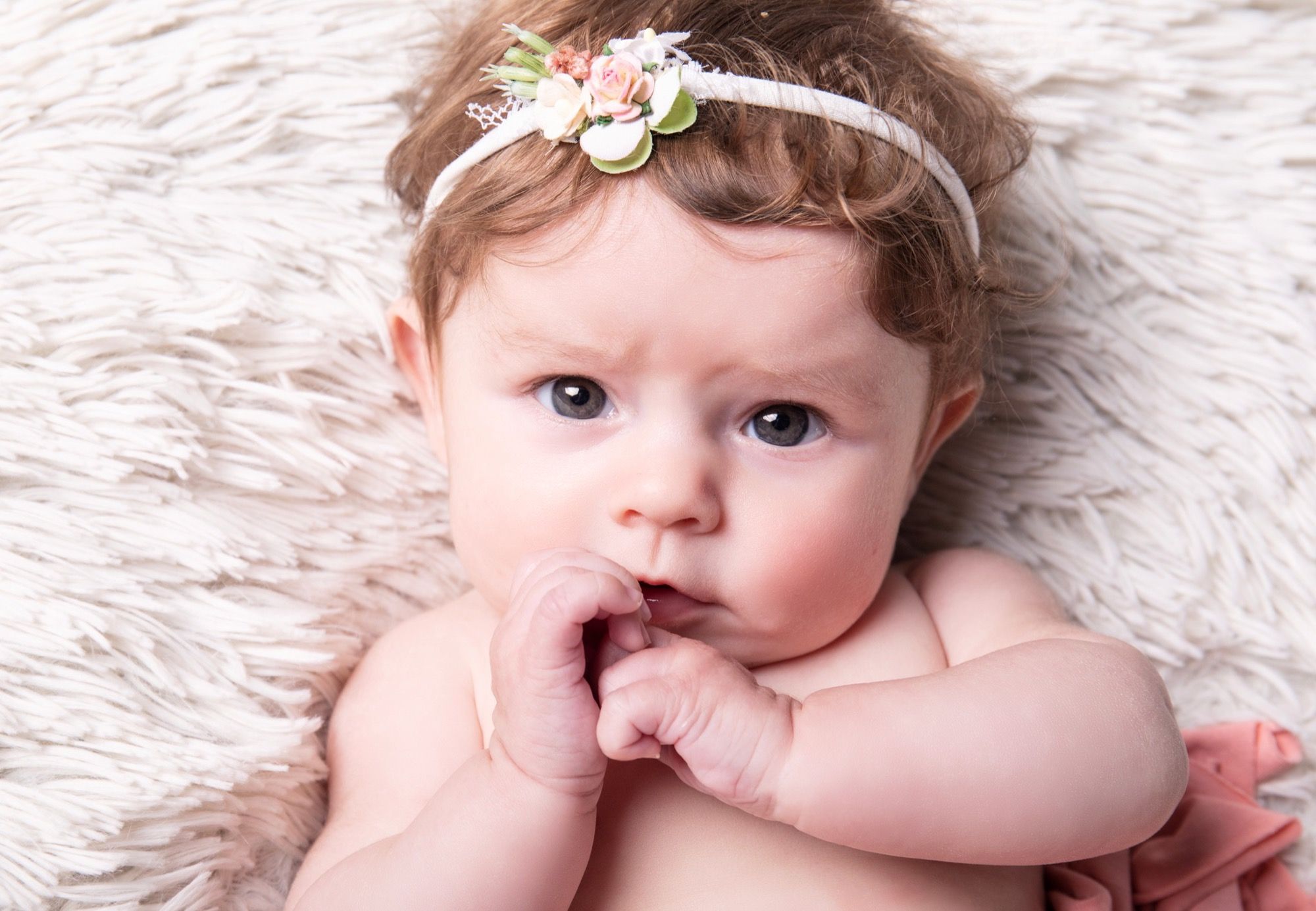 Baby with a flower headband lying on a soft fur, baby photo session at the studio