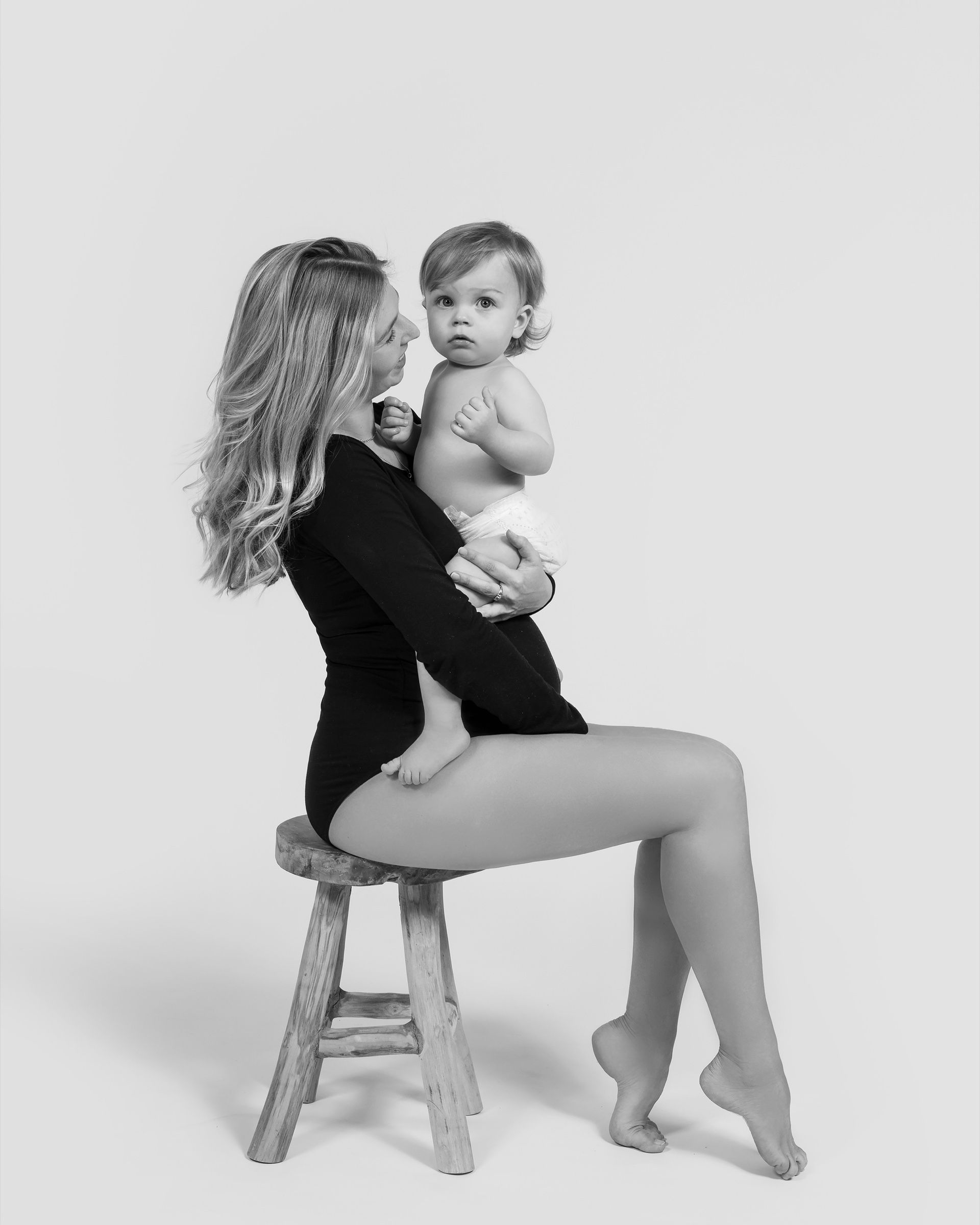 Mère assise sur un tabouret tenant son bébé dans les bras, portrait en studio, noir et blanc