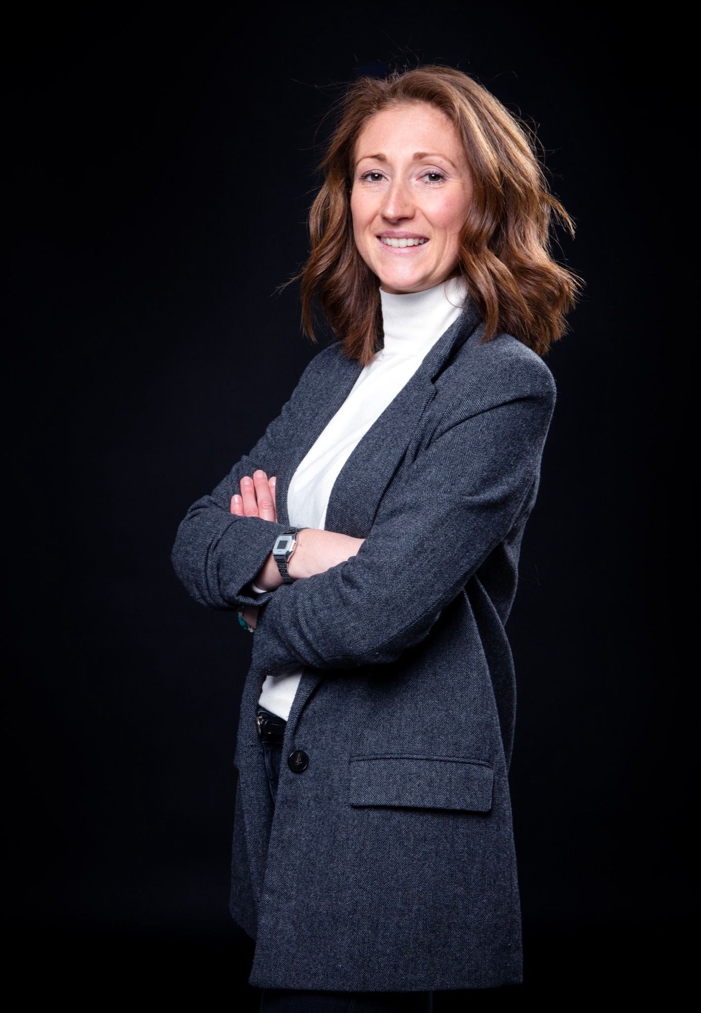 Portrait corporate d'une femme souriante en blazer, bras croisés, sur fond noir au studio