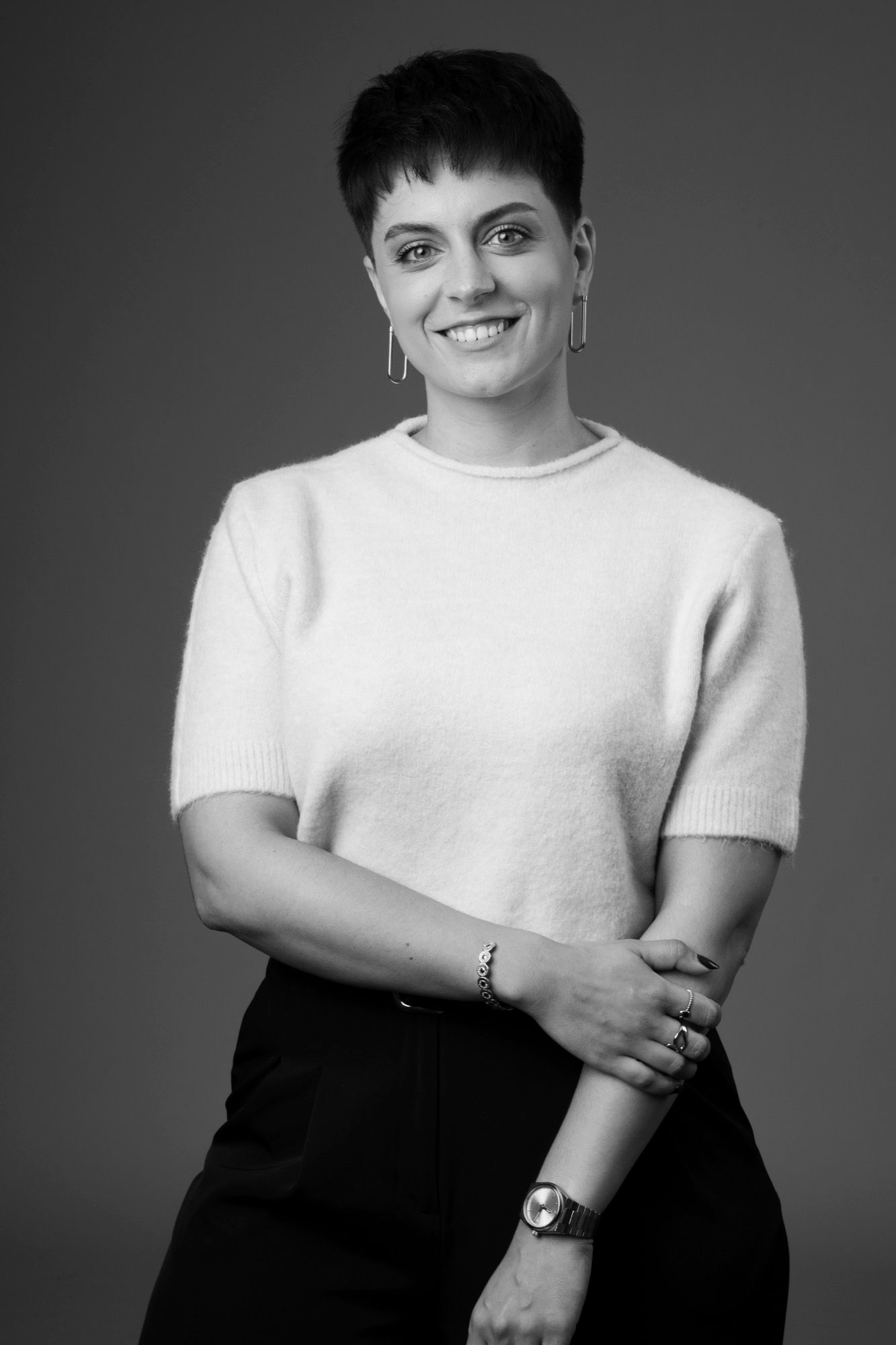 Portrait corporate d'une femme souriante en pull clair, cheveux courts, sur fond gris au studio