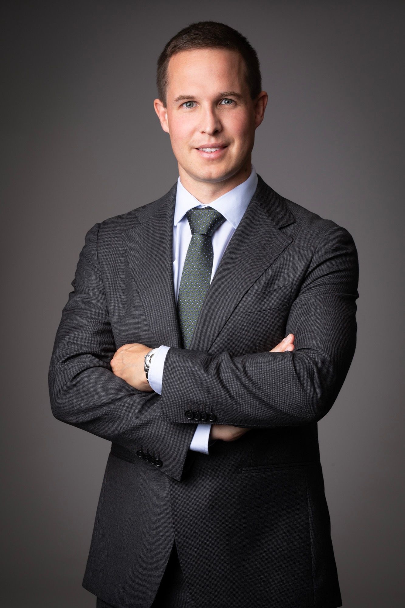 Portrait corporate d'un homme en costume et cravate, bras croisés, sur fond gris au studio