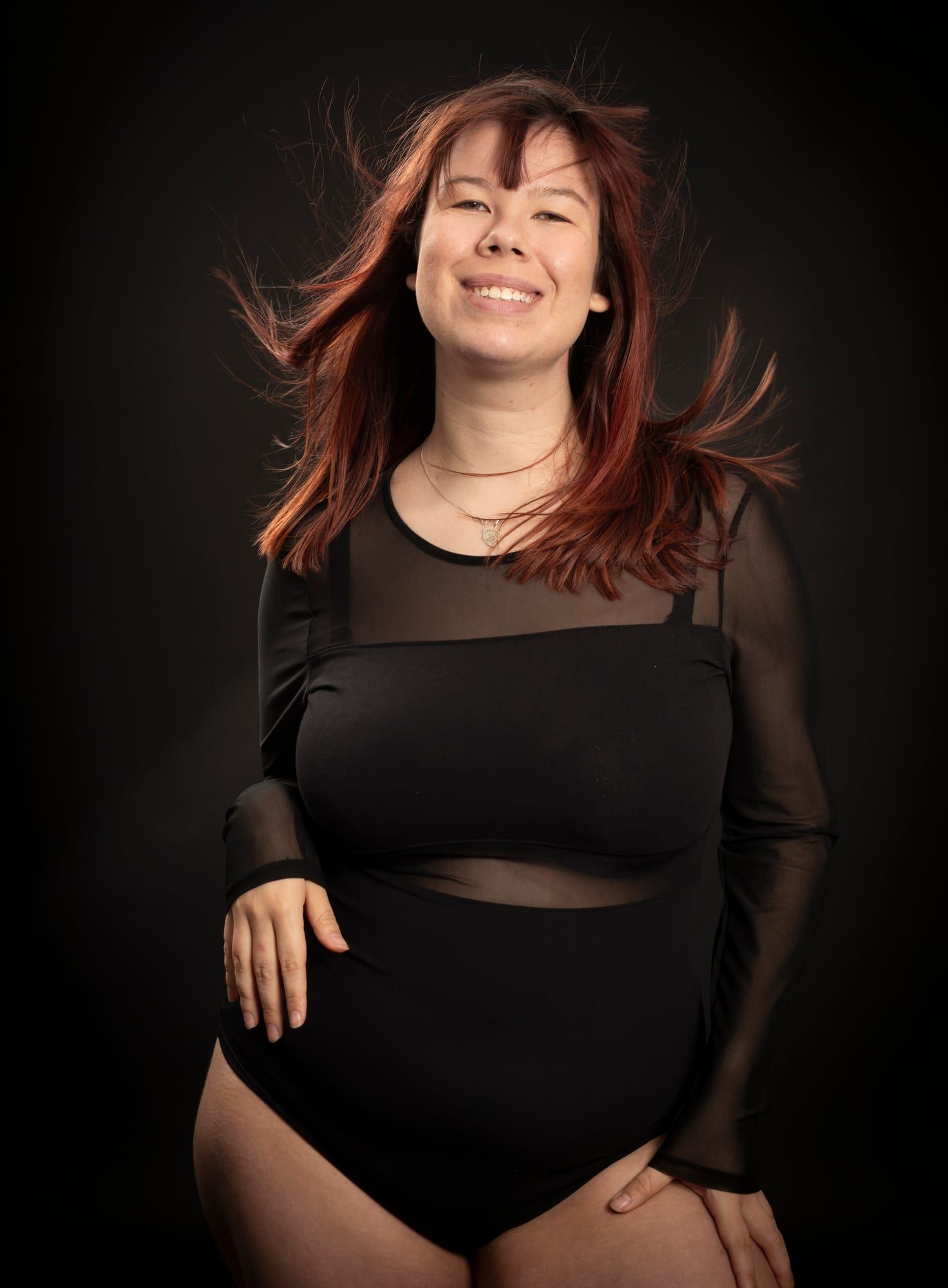 Femme souriante aux longs cheveux roux, portrait en couleur sur fond sombre au studio