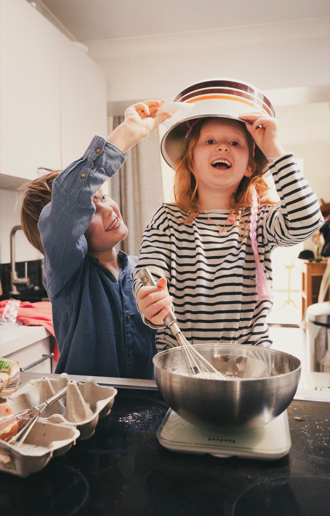 Mother and daughter laughing while baking a cake in the kitchen, family photo session at home