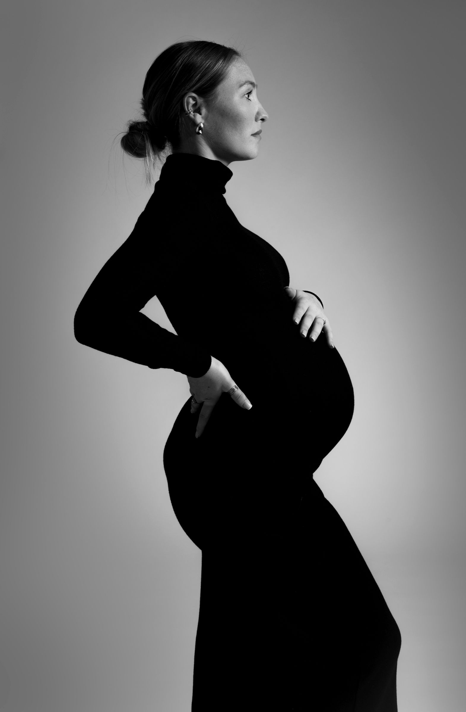 Future maman de profil en robe noire, portrait de grossesse épuré en noir et blanc en studio