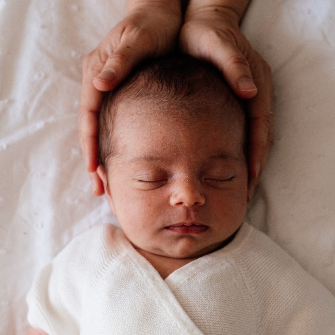 Nouveau-né endormi, les mains de ses parents autour de sa tête, séance naissance à domicile