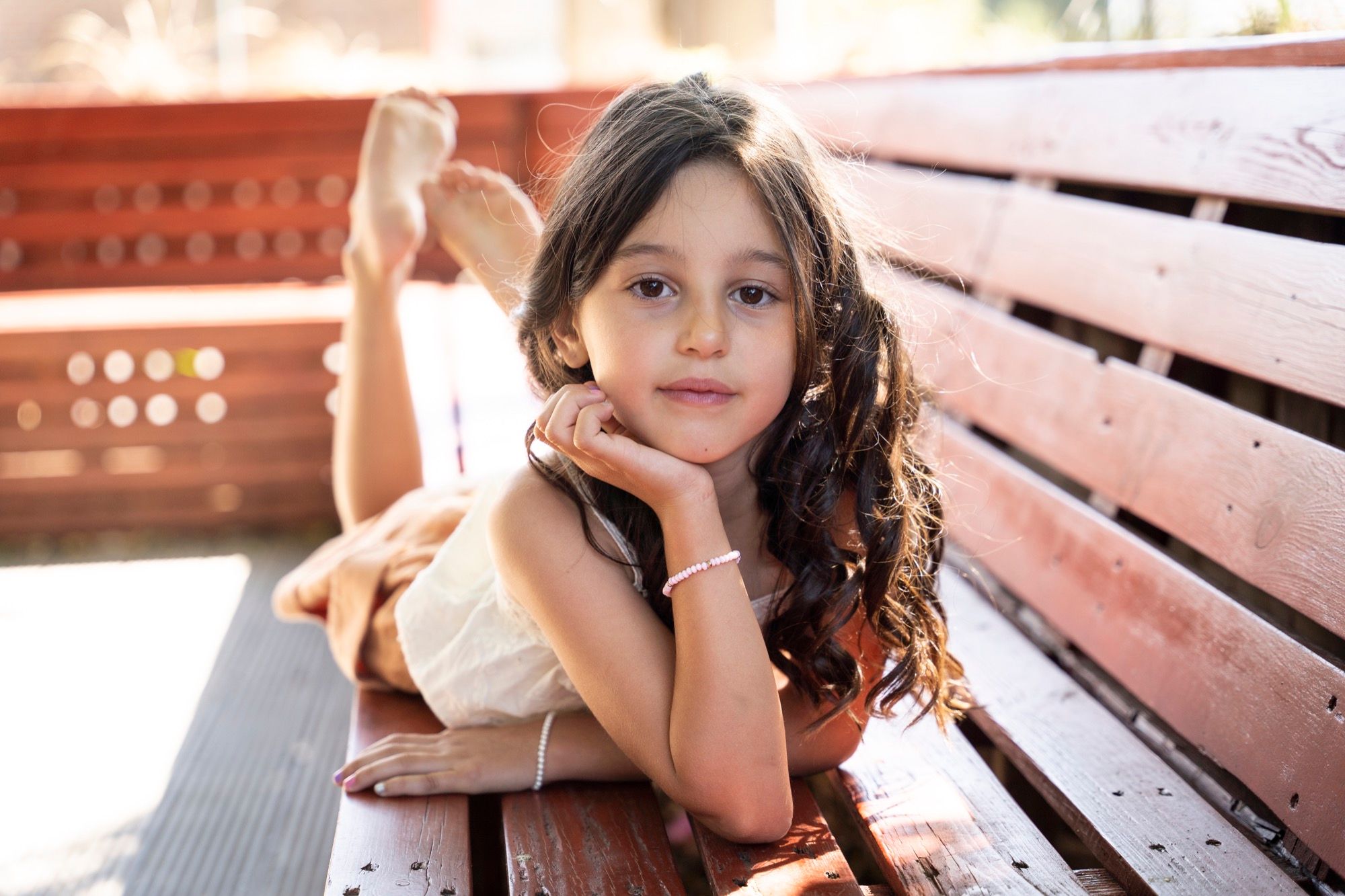 Little girl lying on a wooden bench, chin in her hand, outdoor child portrait