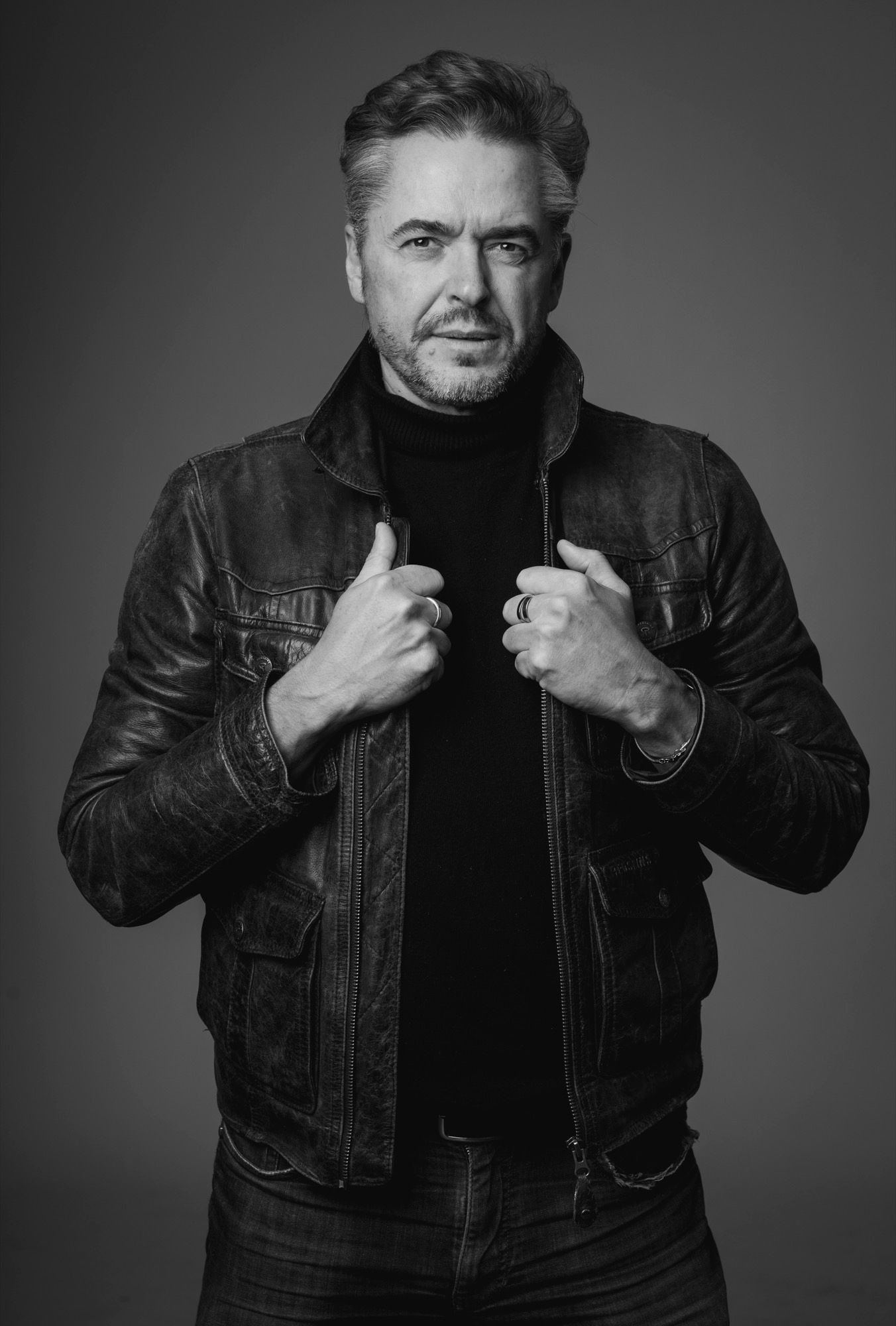 Man in a leather jacket and black turtleneck, black and white portrait on a dark studio background